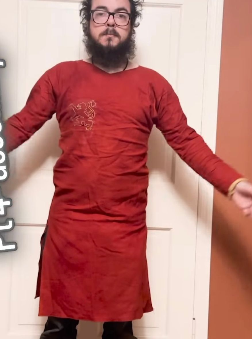Nick, modeling a bright red Medieval-stype hand-made tunic made of hand-dyed red wool, with some gold trim at the wrists and an embroidered gold lion across the chest